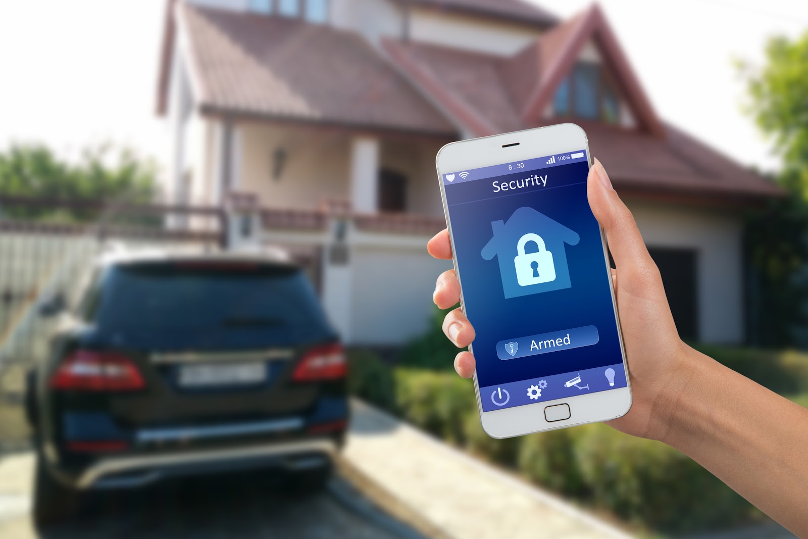 Smartphone with home security app in a hand with a home in the background